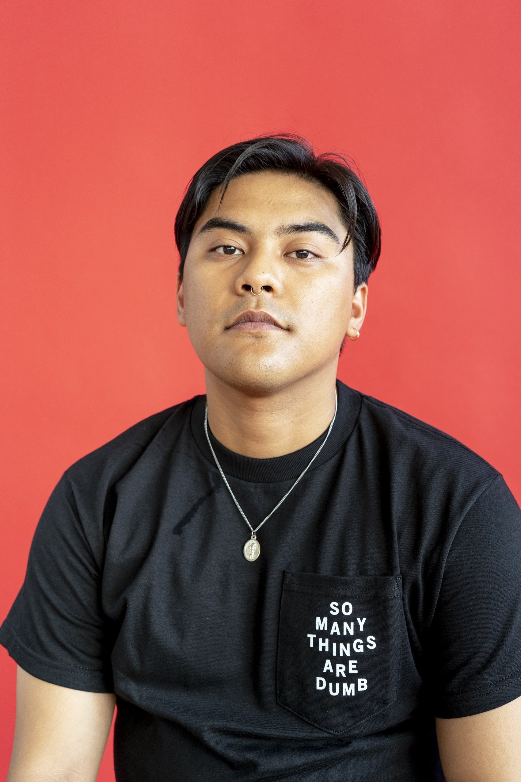 A male model wearing the original NO FUN® "So Many Things Are Dumb" Pocket tee, designed and printed in Toronto. T-shirt features front pocket and white text that reads "SO MANY THINGS ARE DUMB".