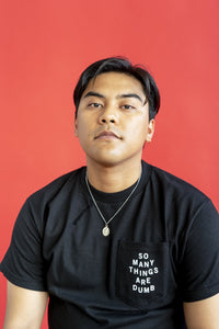 A male model wearing the original NO FUN® "So Many Things Are Dumb" Pocket tee, designed and printed in Toronto. T-shirt features front pocket and white text that reads "SO MANY THINGS ARE DUMB".