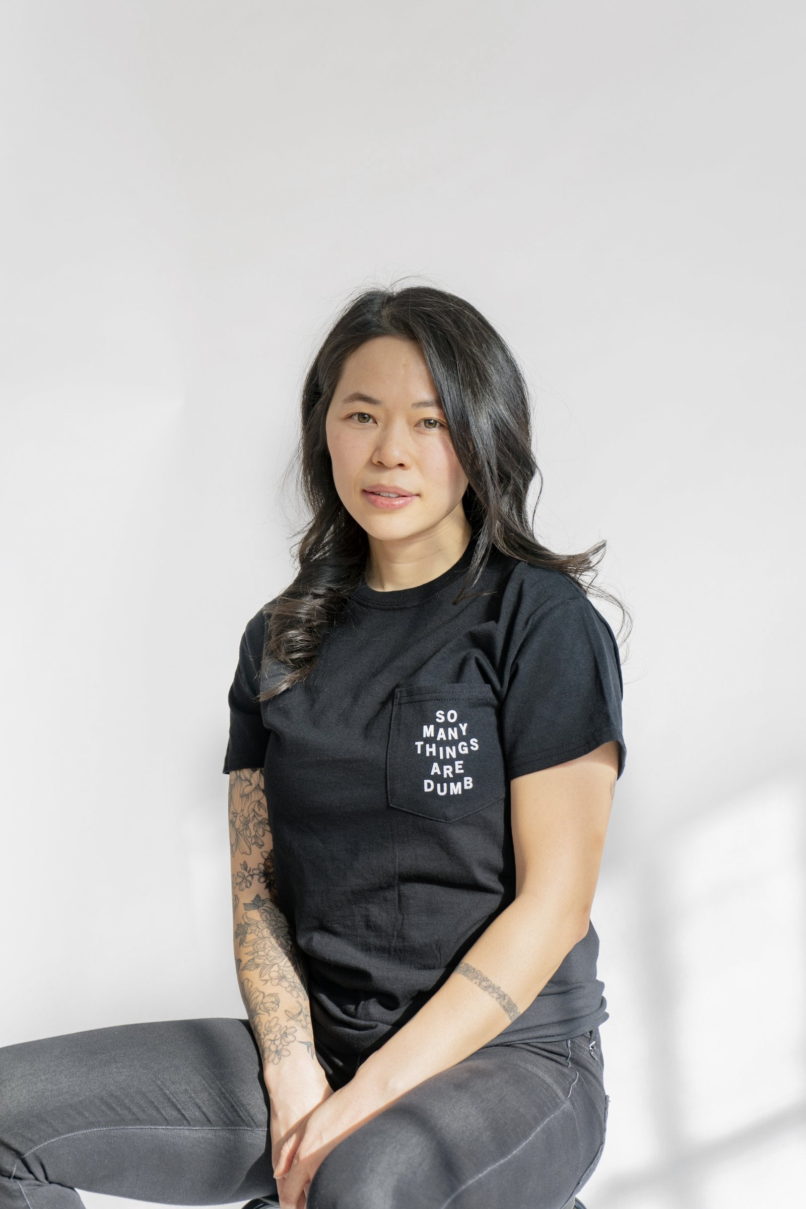 A female model wearing the original NO FUN® "So Many Things Are Dumb" Pocket tee, designed and printed in Toronto. T-shirt features front pocket and white text that reads "SO MANY THINGS ARE DUMB".