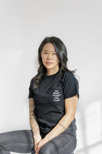 A female model wearing the original NO FUN® "So Many Things Are Dumb" Pocket tee, designed and printed in Toronto. T-shirt features front pocket and white text that reads "SO MANY THINGS ARE DUMB".
