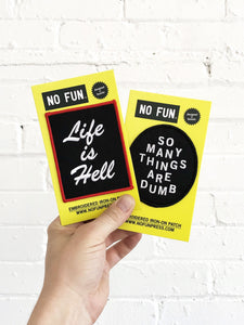 Official "NO FUN®" patch which reads "LIFE IS HELL". The patch features white, embroidered text with a red embroidered edge.  The patch is showcased with our "SO MANY THINGS ARE DUMB" patch with a hand for scale.