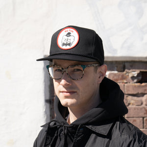 Photo of the "NO FUN®" X "Crawling Death" collaboration black, strapback hat.  The hat features a white patch with red embroidered border.  The embroidered graphic on the patch is a black and white executioner, with red "NO FUN®" logo.