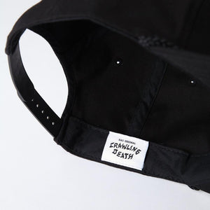 Photo of the "NO FUN®" X "Crawling Death" collaboration black, strapback hat. The hat features a white patch with red embroidered border. The embroidered graphic on the patch is a black and white executioner, with red "NO FUN®" logo.  The photo shoes the inside "Crawling Death" logo.