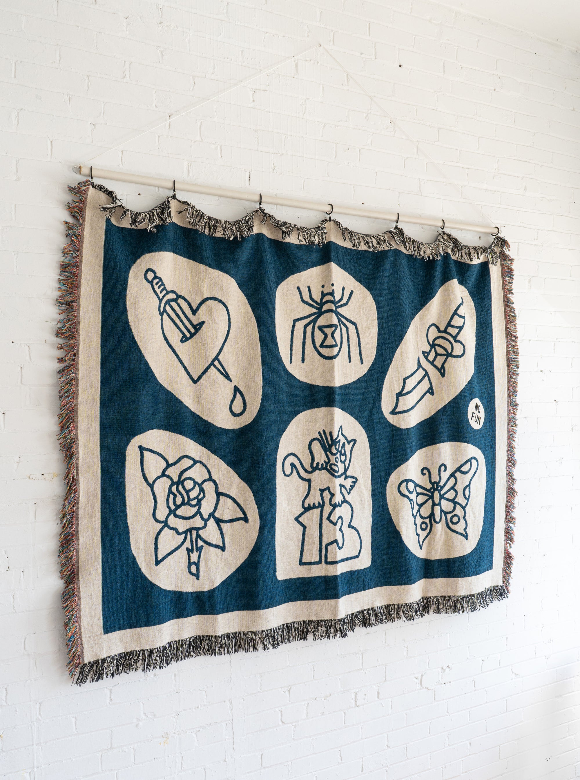 The No Fun® "Flash Sheet" Woven Blanket.  Blanket is hanging from a curtain rod which is mounted to a white cinder block wall.