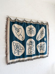 The No Fun® "Flash Sheet" Woven Blanket.  Blanket is hanging from a curtain rod which is mounted to a white cinder block wall.